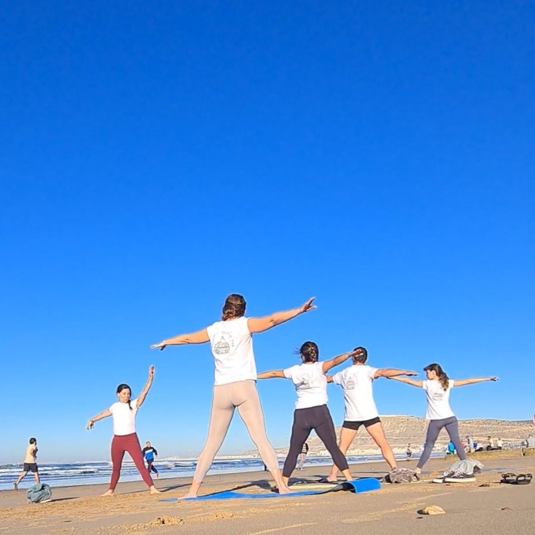 alumnos de holistic yoga practicando en la playa